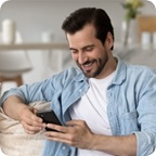 Man sits on couch, smiles at his cell phone. 